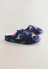 Marinblåa tofflor med en mjuk, plyschig insida och ett mönster av färgglada fåglar som bär olika kläder. Rundad form och platt sula.