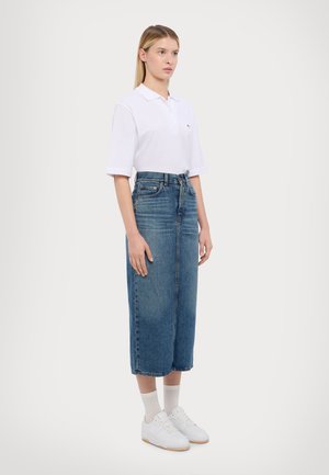 Hvit kortermet polo-skjorte, høy midje blå denimskjørt, hvite joggesko og anklestømper. Enkelt design og avslappet passform.