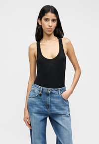 Μαύρο αμάνικο κορμάκι με λαιμόκοψη scoop, με μικρή λεπτομέρεια λογοτύπου. Συνδυάζεται με ψηλόμεσο τζιν παντελόνι σε ανοιχτό μπλε χρώμα.