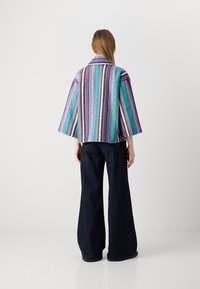 Veste rayée multicolore avec un large col et des manches cloche, fabriquée en tissu léger. Associée à un pantalon en denim foncé taille haute.
