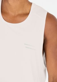 Letvægts, off-white, ærmeløs atletisk tanktop med tekstureret stof og et subtilt grønt accentdesign på brystet.