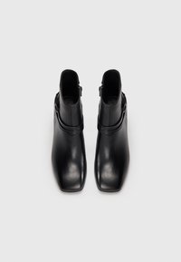 Black leather ankle boots with a square toe, smooth texture, side zippers, and a round strap accent around the ankle.
