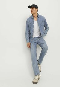 Svetlo modra denim srajca z dvema sprednjima žepoma, bela majica pod njo, svetlo modri jeansi in bež superge z črnimi detajli. Na glavi je črna kapa.