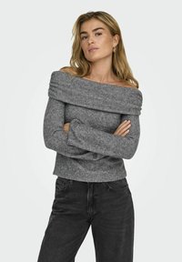 Grauer, schulterfreier Strickpullover mit langen Ärmeln und strukturiertem Finish, kombiniert mit schwarzen Jeans.