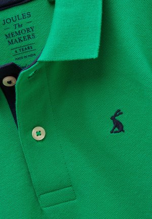 Roheline polosärk tumesinise jänese logoga, kreemjad nööbid ja tekstidega silt, mis ütleb "Joules The Memory Makers 6 Years Made in India."