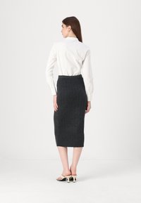 Donkergrijze geribbelde gebreide rok met een aansluitend ontwerp, midi-lengte, gecombineerd met een witte blouse met knopen en beige haksandalen.