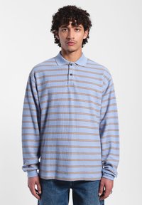 Lange mouwen polo shirt in lichtblauw met horizontale tan strepen. Heeft een kraag en een knoopsluiting. Getextureerde stof.