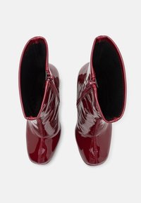 Paire de bottines rouges foncées brillantes avec des bouts carrés et des fermetures éclair latérales, vues de dessus sur fond blanc.