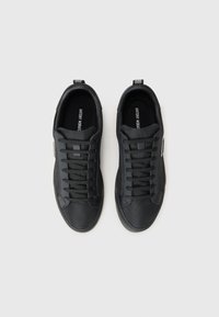 Schwarze Sneaker mit einem strukturierten Obermaterial aus Textil, flachen Schnürsenkeln und einer glatten Gummisohle. Mit einem Logo auf der Zunge und einer Schlaufe hinten.
