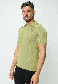 Polo à manches courtes, en maille côtelée, de couleur vert clair, avec un col classique et une coupe ajustée, fabriqué à partir d'un matériau en tricot texturé.