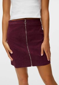 Bordeaux corduroy mini-jurk met een zilveren rits aan de voorkant en een ringtrekker. Heeft een zachte textuur en een getailleerde pasvorm.