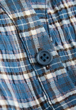 Blauw en crèmekleurig geruit stof met een knoopdetail. Het materiaal is lichtgewicht en gestructureerd, met donkere bruine accenten in het patroon.