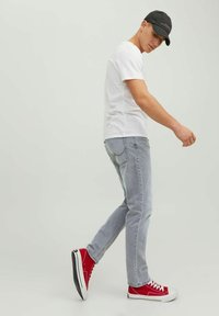 T-shirt blanc, jeans gris clair et baskets rouges. L'ensemble présente un design décontracté, avec une coupe ajustée et peu de détails.