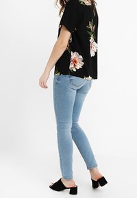 Black short-sleeve top with floral pattern, paired with light blue skinny jeans and black open-toe heels.