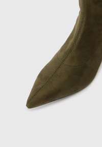 Maslinasto zelena antilop čizma do gležnja s šiljatim vrhom, koja se odlikuje elegantnim dizajnom i vidljivim šavovima duž šavova.