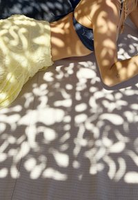 Gelbes, strukturiertes Stoffmaterial liegt über einer hellen Fläche und wirft komplexe Schatten. Ein blauer Stoff mit Verzierungen ist teilweise sichtbar.