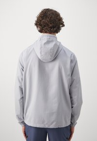 Lichtgrijze, capuchonjas met elastische boorden en zoom. Glad oppervlak, eenvoudig ontwerp zonder zichtbare patronen of hardwaredetails.