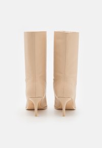 Beige nahka nilkkasaappaat, joissa on terävä kärki ja ohuet korot. Sileä pinta, minimalistinen muotoilu ja pystysuorat ompeluyksityiskohdat.