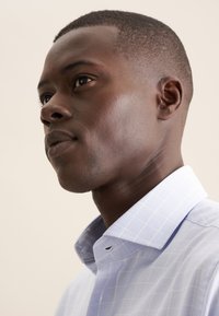 Camicia a quadri blu con colletto alla francese, realizzata in tessuto leggero. Presenta un motivo a griglia sottile e orlo arrotondato.