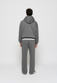 Grauer Hoodie mit einer großzügigen Kapuze, abgesenkten Schultern und einer Kängurutasche, kombiniert mit passenden grauen Sweatpants mit einer Gesäßtasche.