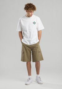 Valkoinen puuvillapaita, jossa on "New York Records" -grafiikka, yhdistettynä polven mittaisiin khaki-kargo-shortseihin, joissa on useita taskuja. Valkoiset lenkkarit.