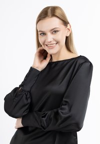 Schwarze Satinbluse mit lockerer Passform, Rundhalsausschnitt, Puffärmeln und Knopfdetails an den Bündchen. Glatte Textur, elegantes Design.