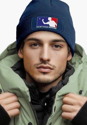 Navy knit beanie with a Major League Beer Pong logo; worn with a green padded jacket over a black inner layer. Textured fabric, snug fit.