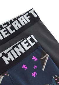 Černé a modré spodní prádlo s širokým páskem s logem Minecraft, na kterém jsou pixelované grafiky v purpurové a šedé na látce.