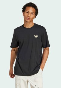 Svart bomull t-shirt med en subtil vit logotyp på bröstet, rundad halsringning och korta ärmar, tillsammans med ljusa byxor.