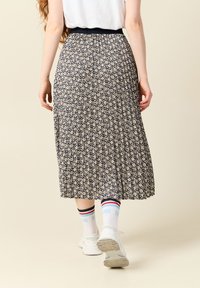 Jupe plissée navy avec un petit motif floral, taille élastique, longueur mi-mollet. Des baskets blanches et des chaussettes à rayures sont portées.
