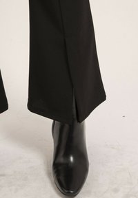 Pantalons noirs sur mesure avec une légère fente à l'ourlet, associés à des bottes noires brillantes à bout pointu et à la silhouette élégante.