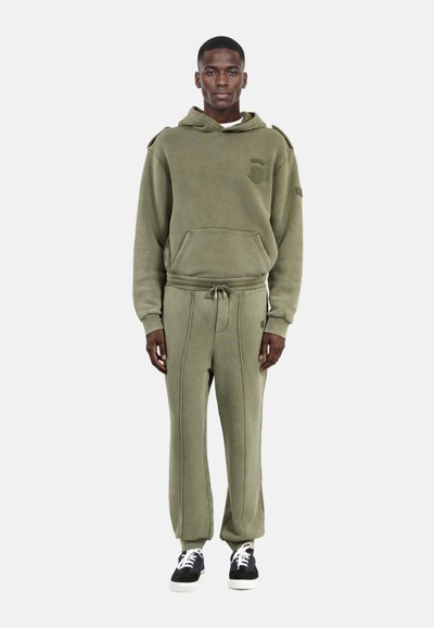 Felpa con cappuccio verde oliva e pantaloni abbinati realizzati in tessuto morbido. La felpa ha una tasca frontale e un logo; i pantaloni presentano un cordino e cuciture verticali.