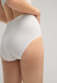 Bílé vysoké kalhotky s hladkým povrchem a kontrastním lemem. Design je minimalistický s bezešvým provedením.