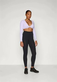 Lila hosszú ujjú crop top, elcsavart elejével, fekete magas derekú leggings-szel párosítva. A leggings sima textúrájú és testhez simuló.