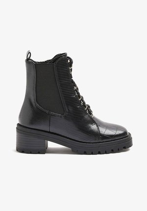 Bottine noire en cuir texturé avec talon épais, lacets sur le devant et panneau latéral élastique pour un enfilage facile.