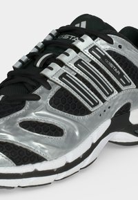 Μαύρο και ασημί αθλητικό παπούτσι Adidas adiSTAR με λεπτομέρειες από δίχτυ, μαύρα κορδόνια και λευκή υφασμένη σόλα.