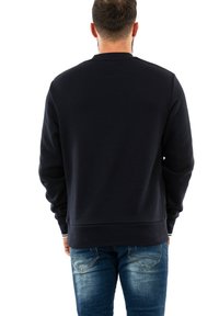 Felpa navy con scollatura rotonda e polsini a costine. Caratterizzata da una consistenza morbida e una vita aderente, abbinata a jeans blu chiaro.