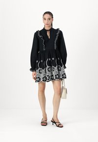 Μαύρο φόρεμα με μακριά μανίκια, ρυθμισμένο λαιμόκοψη και κεντημένο άσπρο λουλουδάτο σχέδιο. Συνδυάζεται με μαύρες λουράτες γόβες και μια μικρή άσπρη τσάντα.