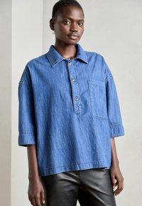 Blaue Jeanshemd mit Kragen, halber Knopfleiste und Brusttasche. Verfügt über kurze, weite Ärmel und eine lockere Passform.