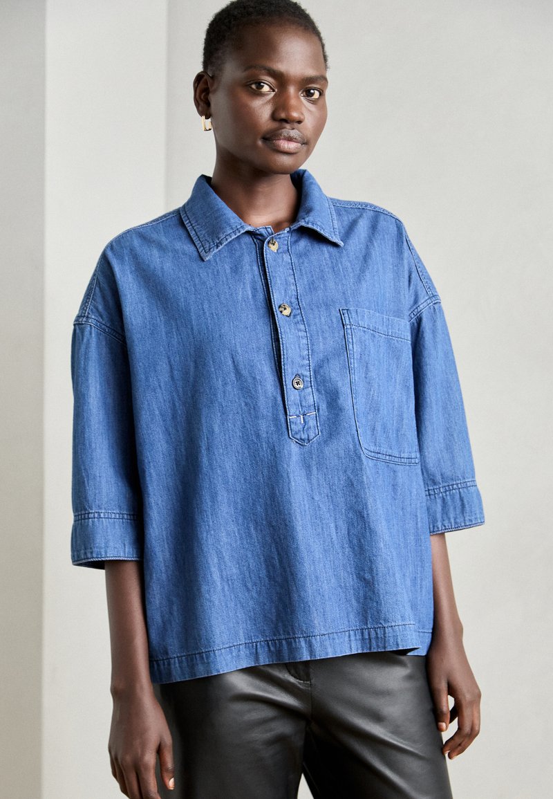 Blaue Jeanshemd mit Kragen, halber Knopfleiste und Brusttasche. Verfügt über kurze, weite Ärmel und eine lockere Passform.