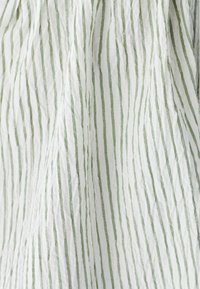 Biela látka s tenkými vertikálnymi zelenými pruhmi a jemnými vráskami vytvárajúcimi textúrovaný vzor.