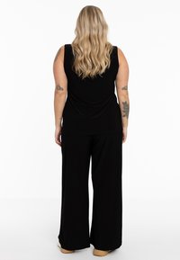 Zwarte mouwloze top gecombineerd met zwarte brede broek. De stof lijkt zacht en er zijn subtiele plooien aan de achterkant van de top.