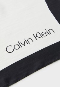 Sorte og hvite silkesquare skjerf med en kontrasterende mørk stripe og "Calvin Klein" trykt i svarte små bokstaver.