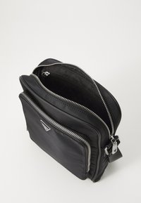 Borsa a tracolla nera in pelle con cerniere argento, più scomparti e una superficie esterna liscia. Presenta una placca con logo sul davanti.