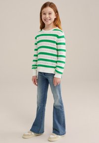 Stickad tröja med vita och gröna horisontella ränder och öppet mönster, kombinerad med ljusblå utsvängda jeans och beige skor.