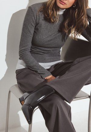 Siva rebrasta majica s dolgimi rokavi je navlečena čez belo turtleneck, v kombinaciji s širokimi sivimi hlačami in bleščečimi črnimi gležnjarji. Vidne so srebrne obroče.