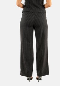 Pantalones de pierna ancha a rayas negras, hechos de tela texturizada, con cintura alta y un ajuste relajado, combinados con zapatos de tacón alto negros.
