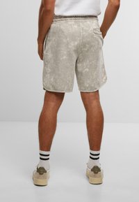 Shorts gris clair avec une texture marbrée, taille élastique, poches latérales et une poche arrière. Portés avec des chaussettes blanches et noires rayées.