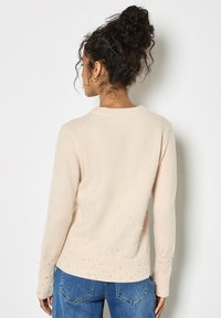 Beiger Strickpullover mit texturiertem Finish, ausgestattet mit dekorativen Perlen und gerippten Bündchen, von hinten präsentiert.