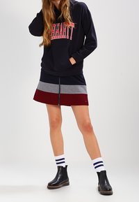 Sudadera navy con el texto "Carhartt", combinada con una falda multicolor con rayas rojas, grises y navy, botas negras hasta el tobillo y calcetas a rayas.